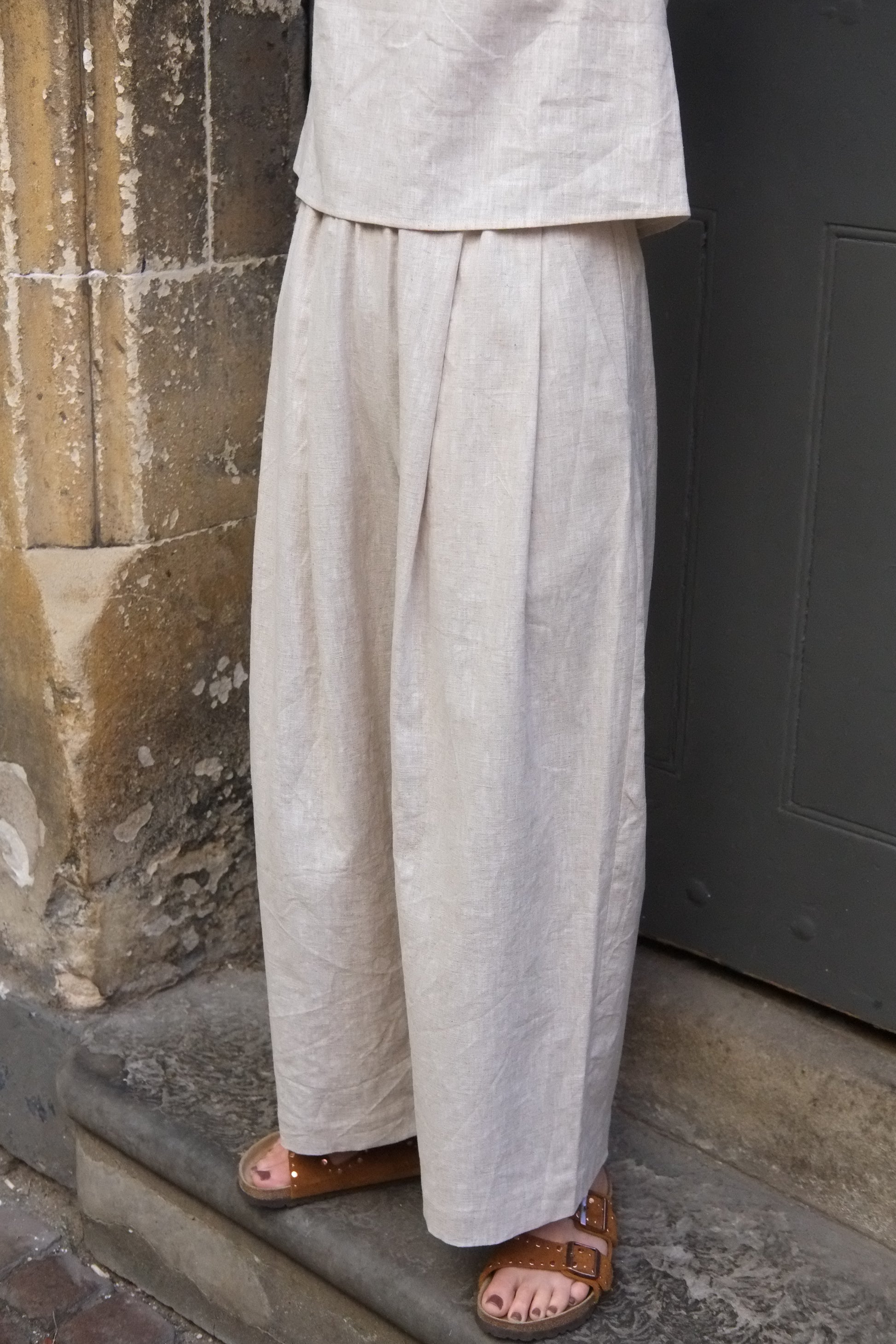 Person wearing light-colored pants and sandals standing on a stone floor.