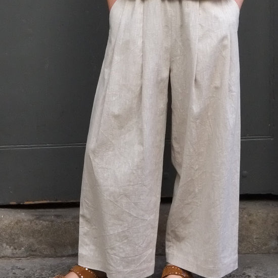 woman wearing cream coloured trousers with hands in pockets and brown sandals