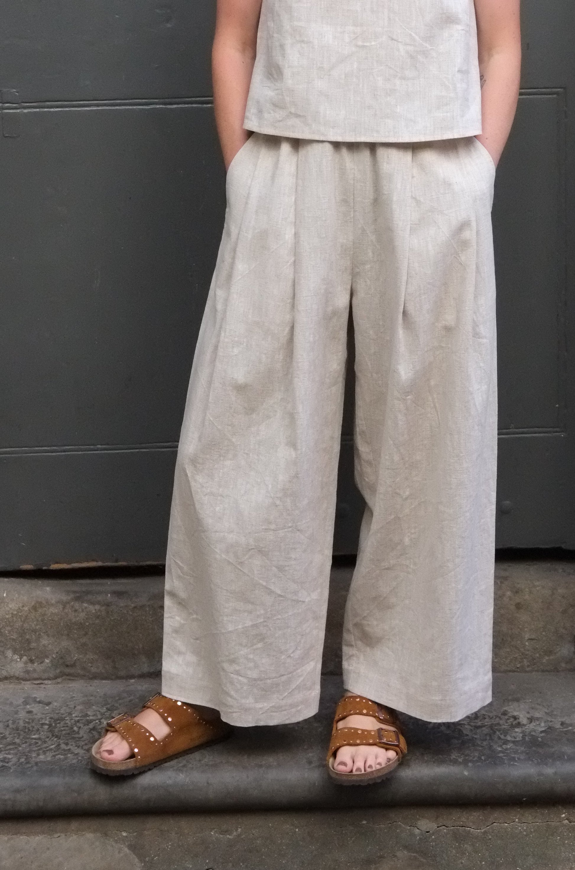 woman wearing cream coloured trousers with hands in pockets and brown sandals