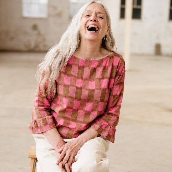 Woman laughing heartily in a room with large windows.