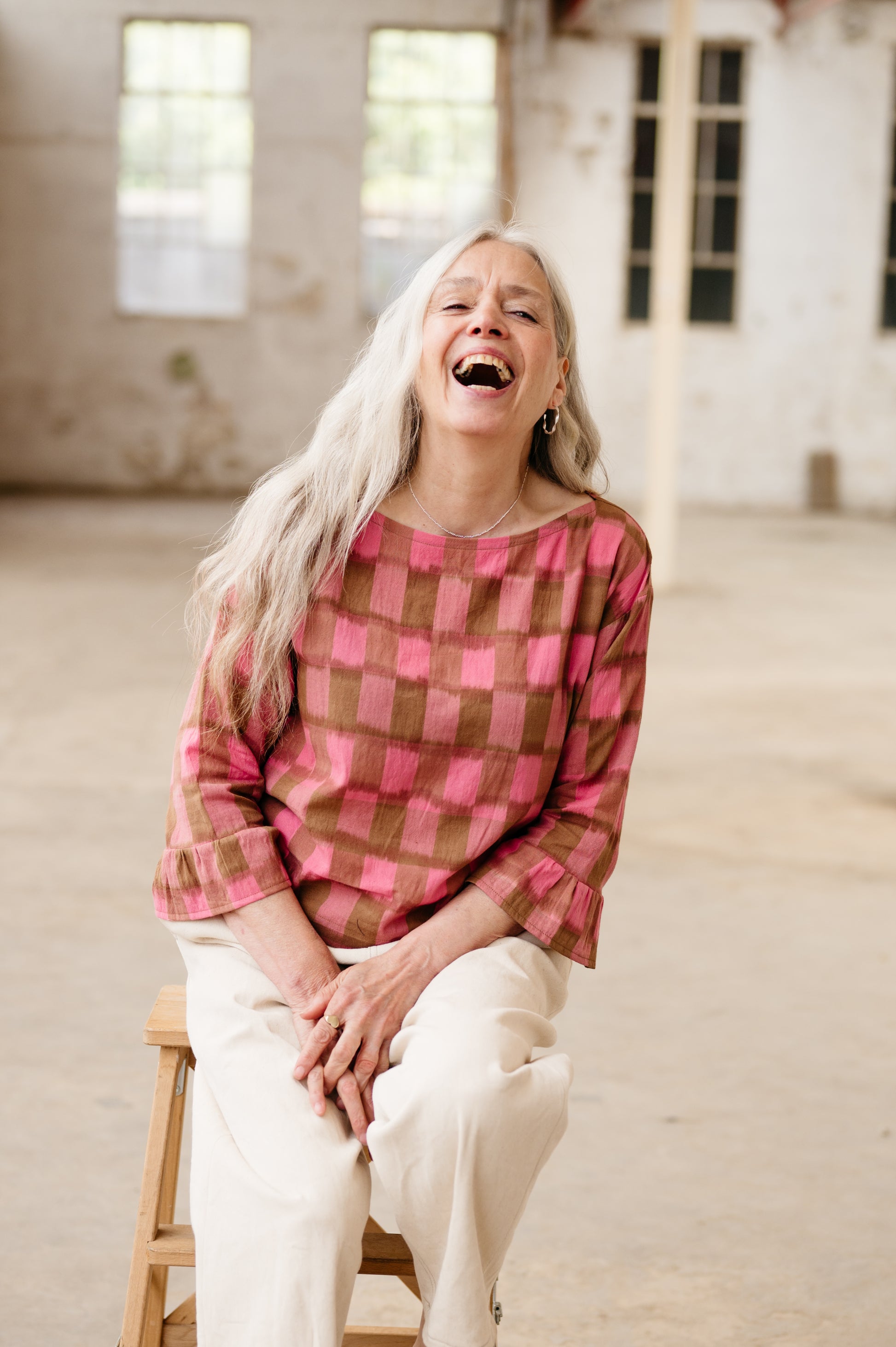 Woman laughing heartily in a room with large windows.