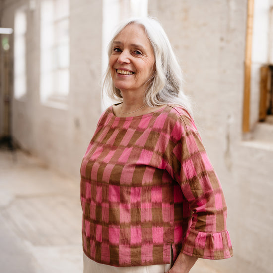 Woman wearing a pink and brown checkered top in an indoor setting