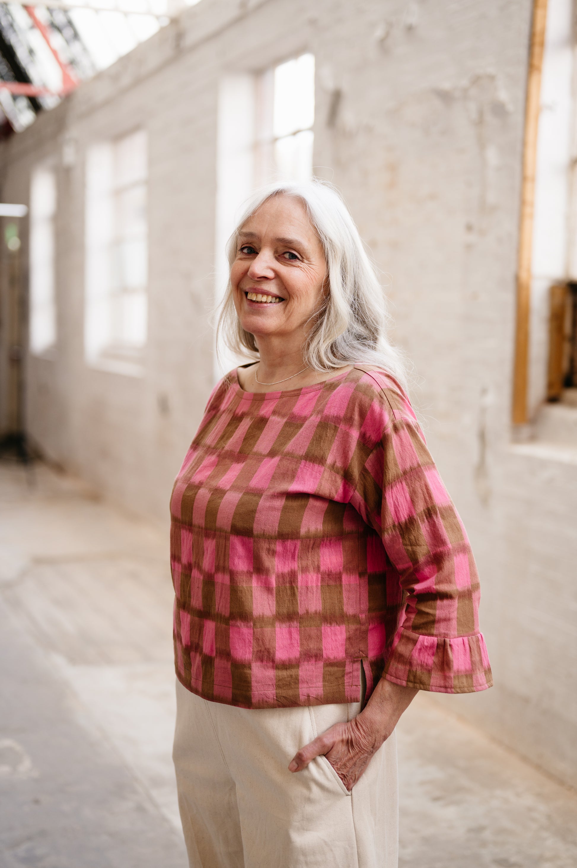 Woman wearing a pink and brown checkered top in an indoor setting
