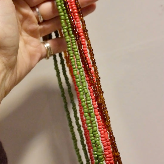 Hand holding a colourful beaded necklaces against a neutral background