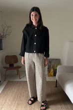 Load image into Gallery viewer, Woman standing in a living room wearing a black workwear jacket and brown gingham trousers.
