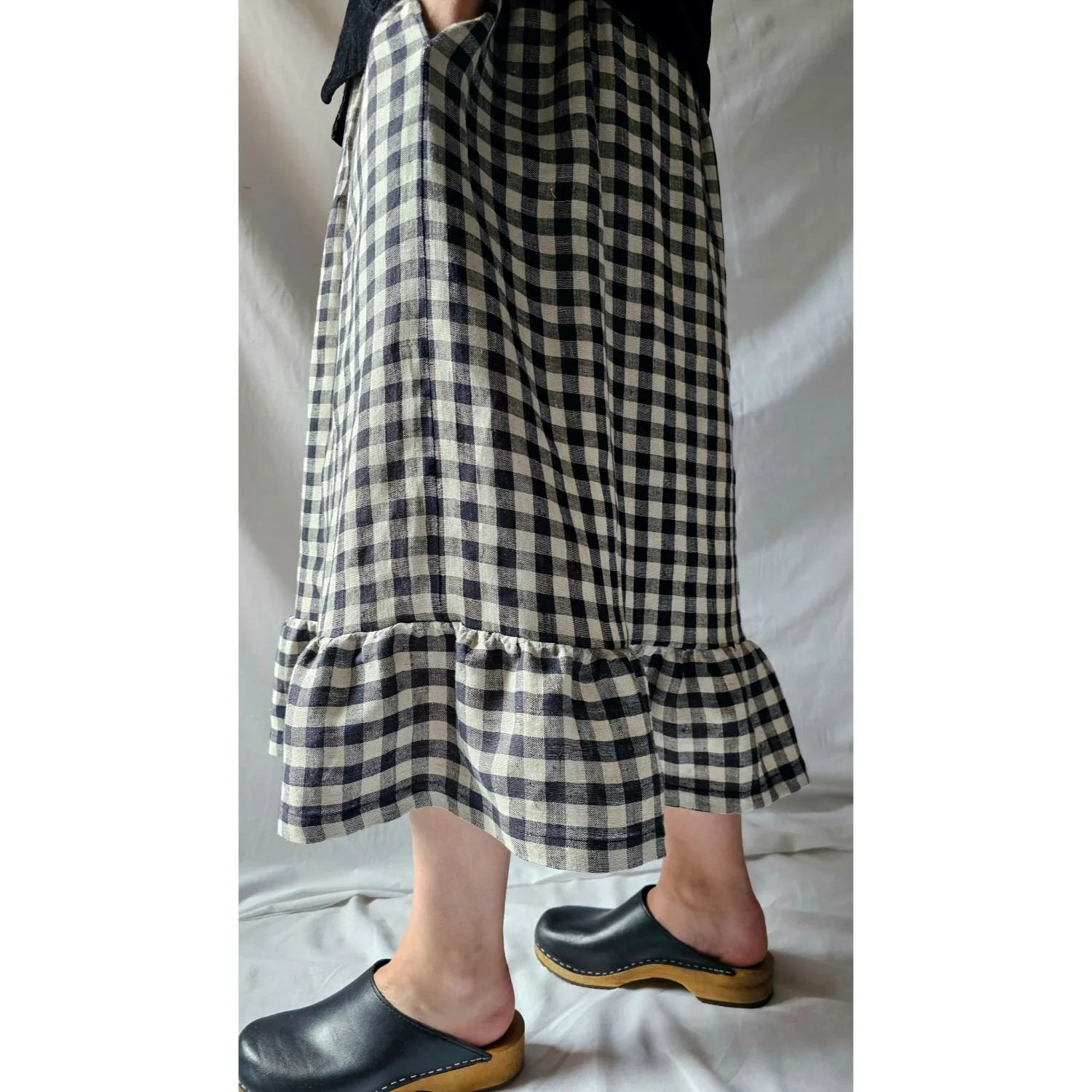 Person wearing a black and white checkered skirt with ruffled hem on a plain background