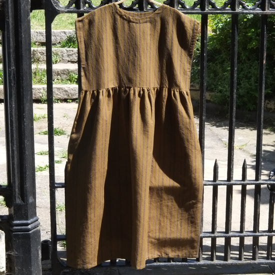 Brown dress hanging on a black metal fence with greenery in the background