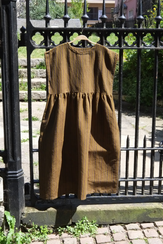 Brown dress hanging on a black metal fence with greenery in the background