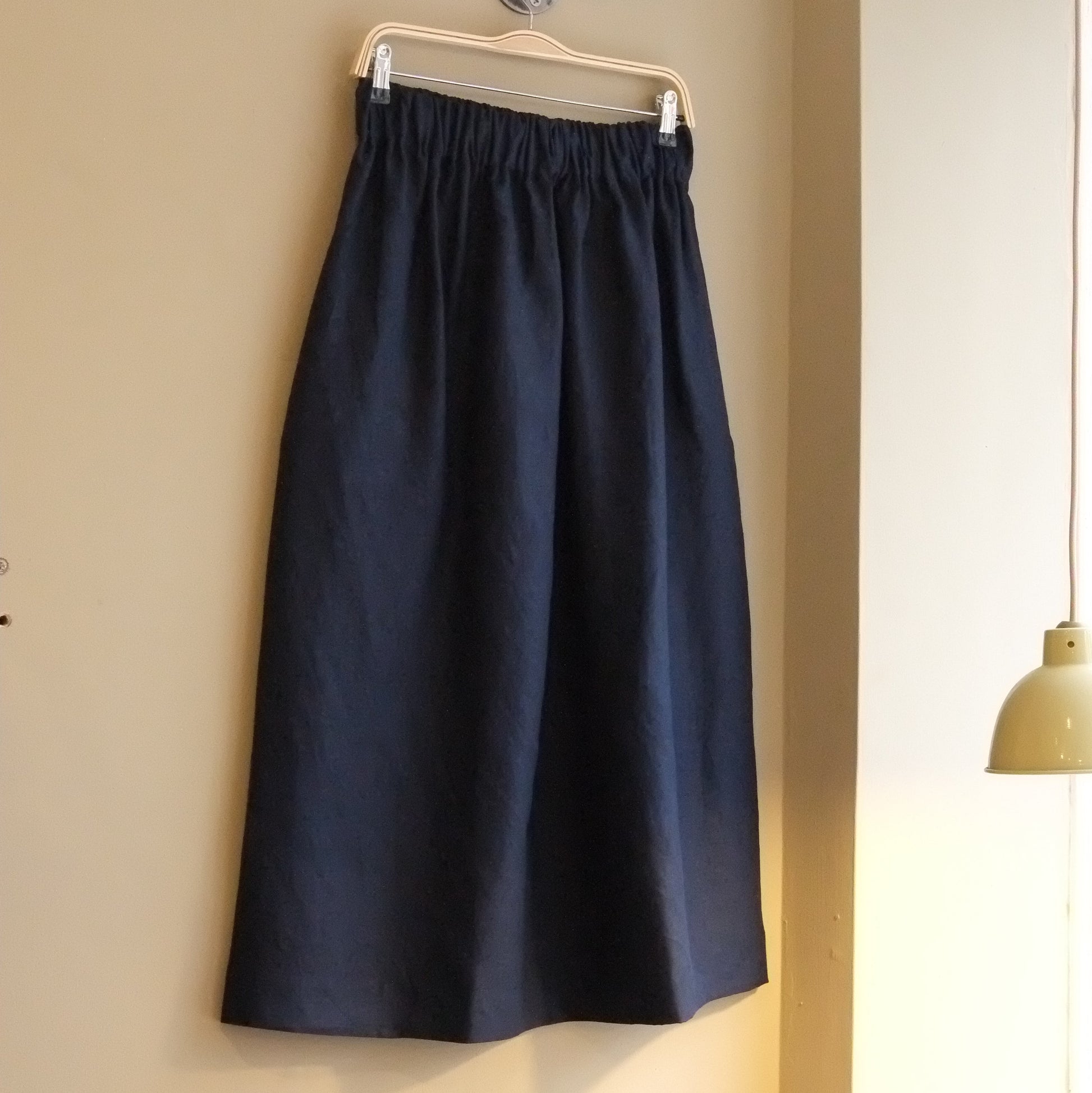 Navy blue skirt hanging on a hanger against a beige wall.