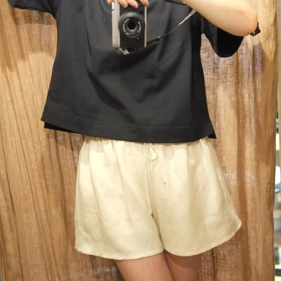 Person holding a camera wearing linen shorts and black boxy t shirt