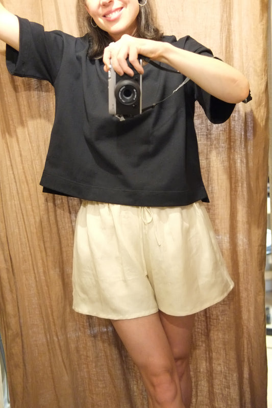 Person holding a camera wearing linen shorts and black boxy t shirt