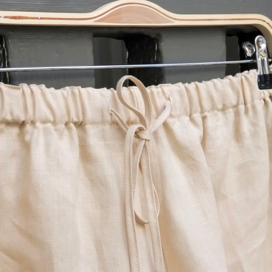 Beige linen shorts on a hanger against a dark background