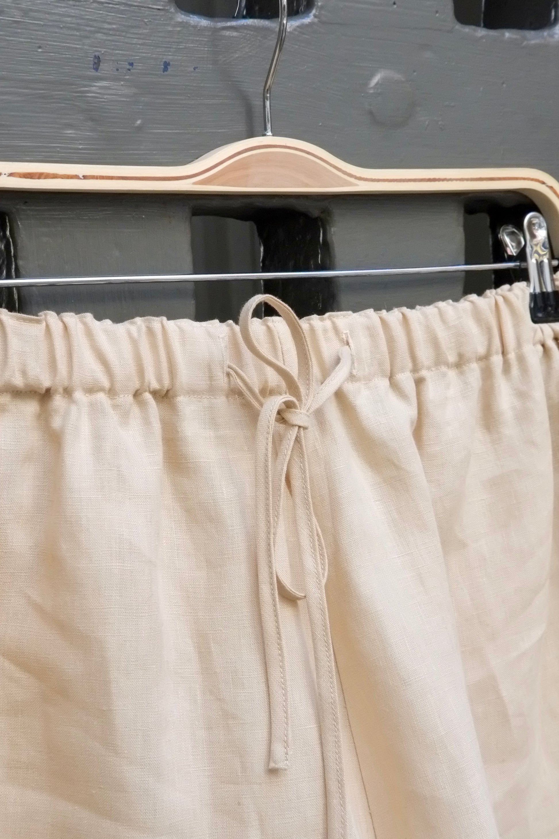 Beige linen shorts on a hanger against a dark background
