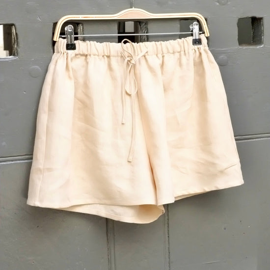 Beige shorts on a hanger against a gray wall with square patterns