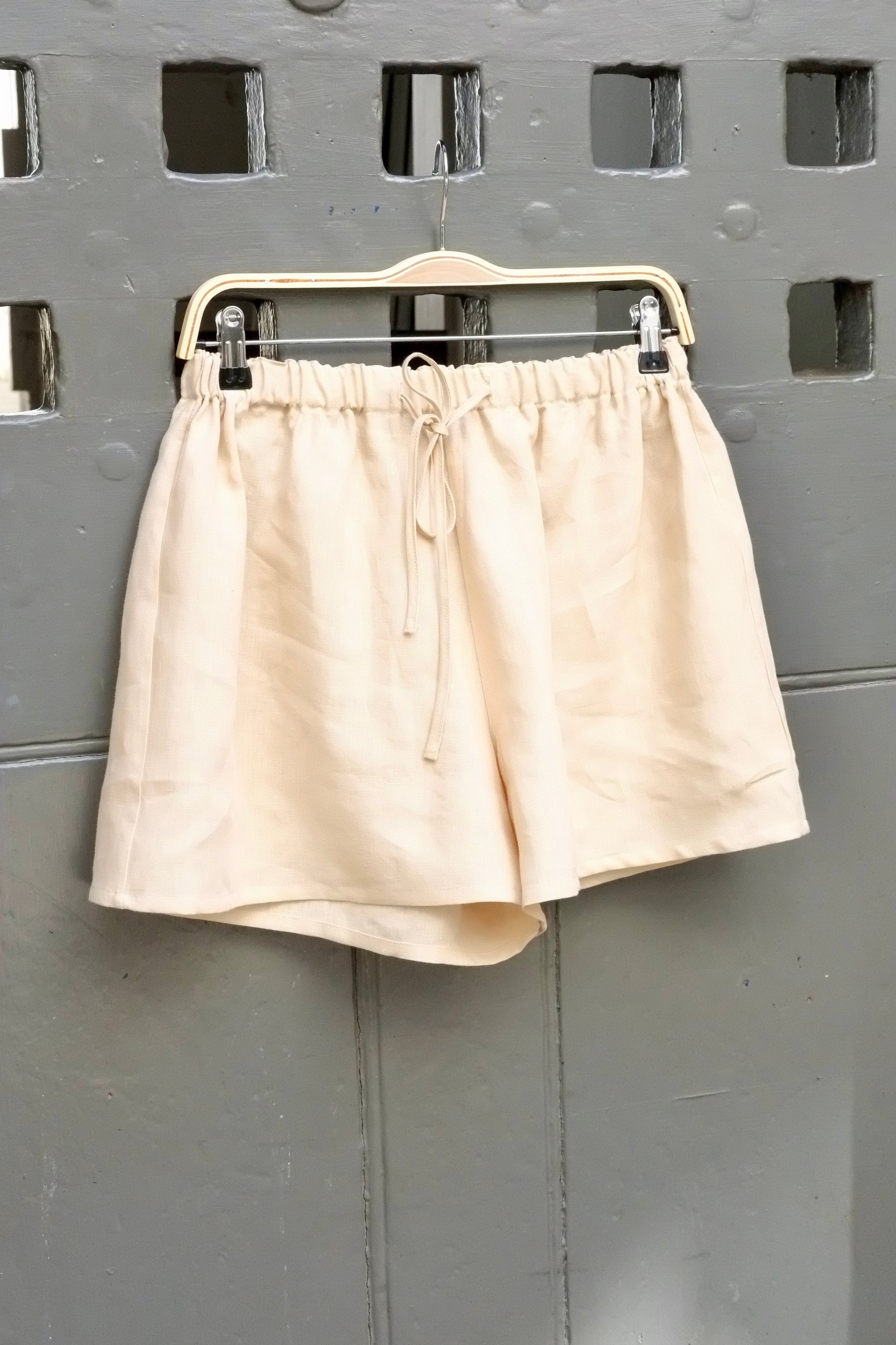 Beige shorts on a hanger against a gray wall with square patterns
