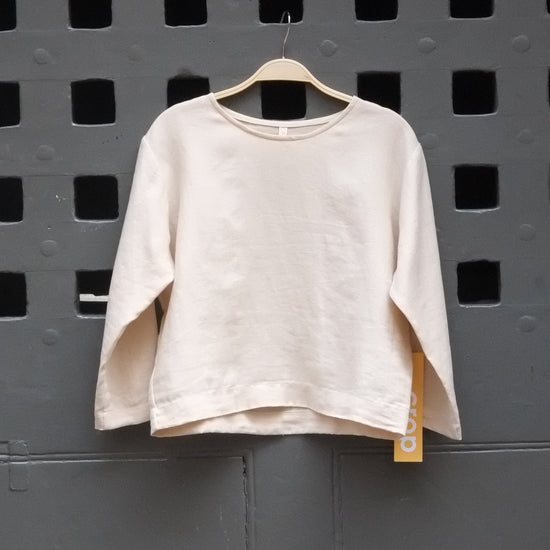 A light beige long sleeve t-shirt hanging on a wooden hanger from a grey grid door.