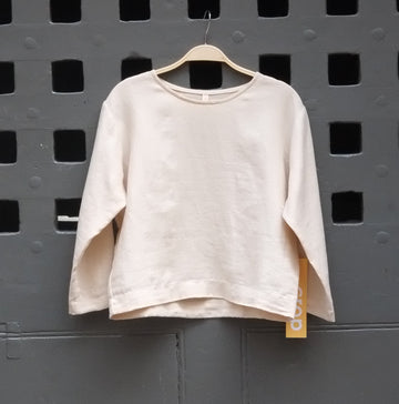 A light beige long sleeve t-shirt hanging on a wooden hanger from a grey grid door.