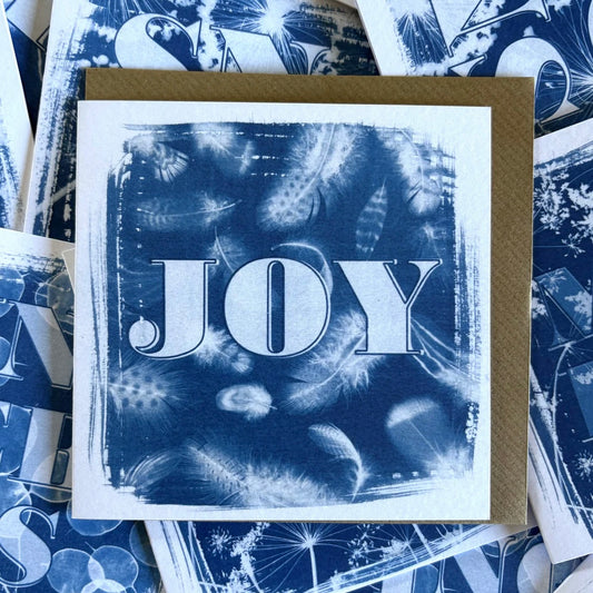 Card with 'JOY' text on a blue feather cyanotype design with a brown envelope, surrounded by more cards with similar designs.