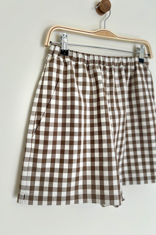 Brown and white checkered shorts on a hanger against a light background
