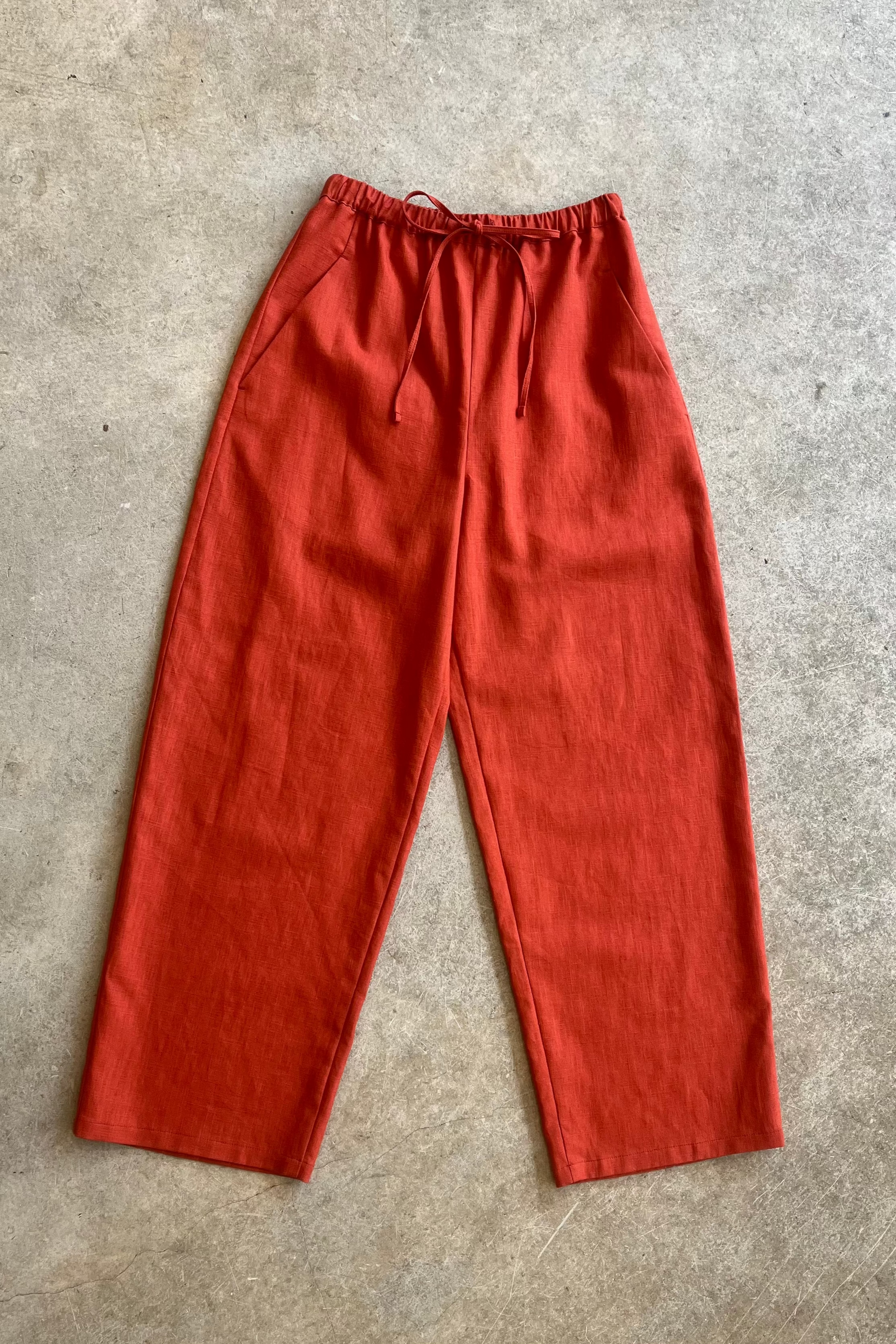 Red linen trousers on a gray concrete floor