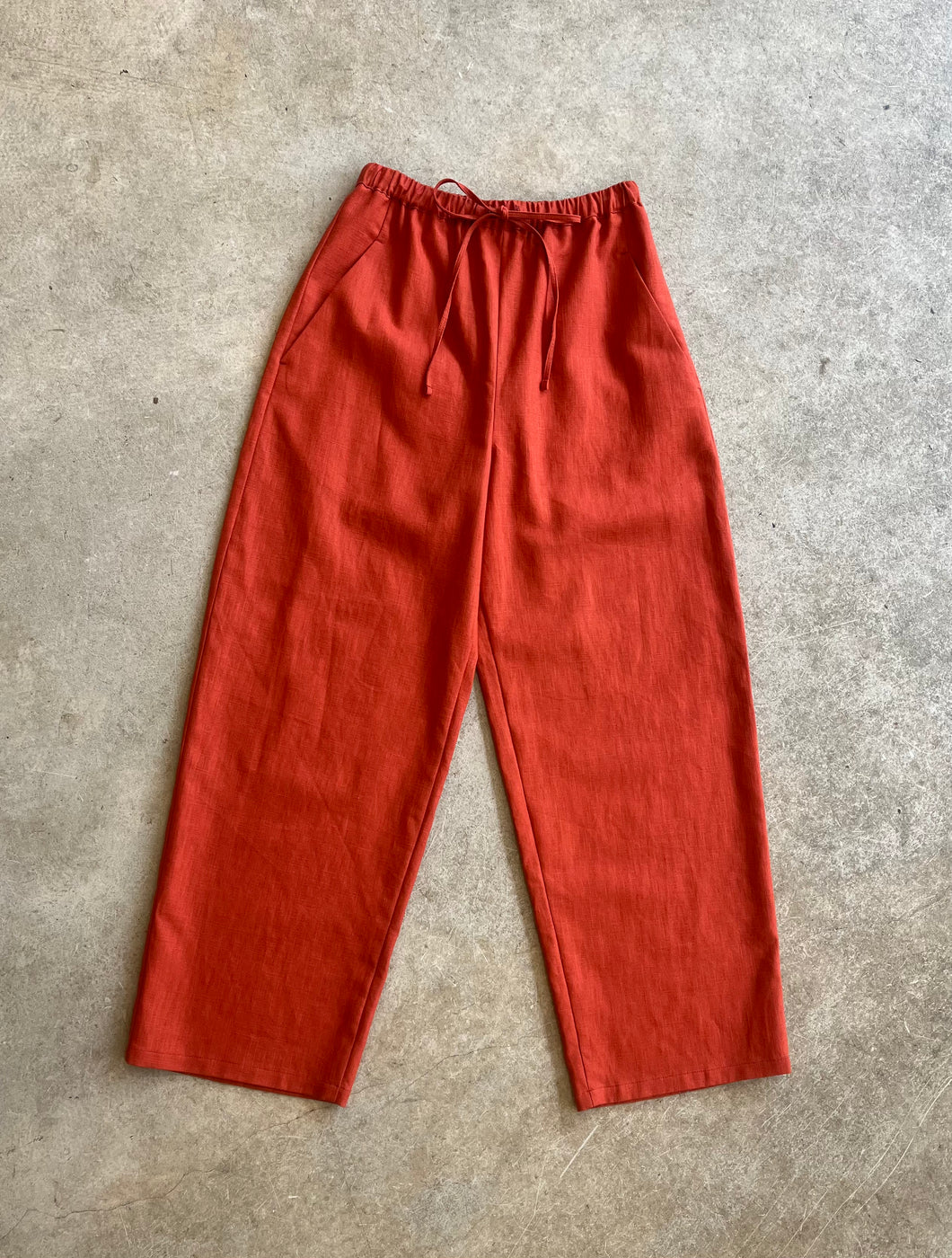 Red linen trousers on a gray concrete floor
