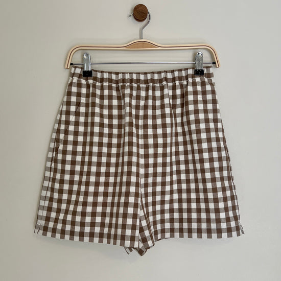 Brown and white checkered shorts on a hanger against a plain background