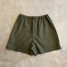 Load image into Gallery viewer, Green linen shorts with an elasticated waistband on a textured beige surface
