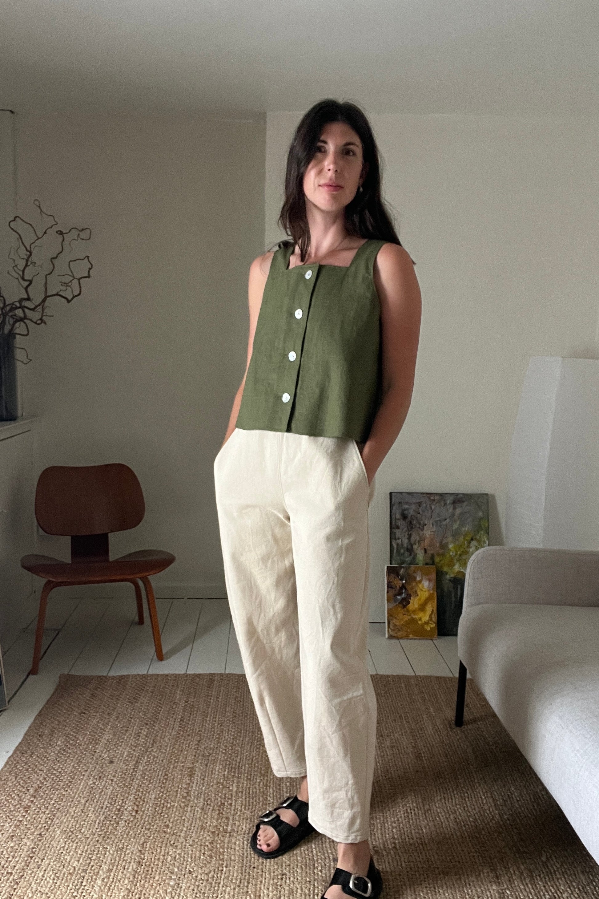 Woman wearing a green sleeveless top and white pants in a living room setting.