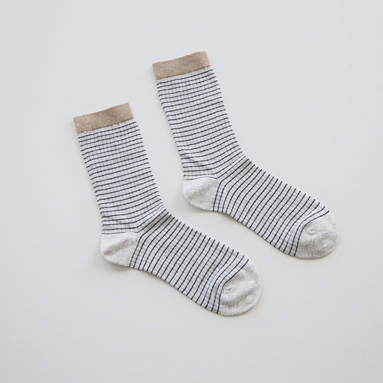 A pair of crew socks with thin black horizontal stripes on a white base, featuring a solid beige ribbed cuff and toe.