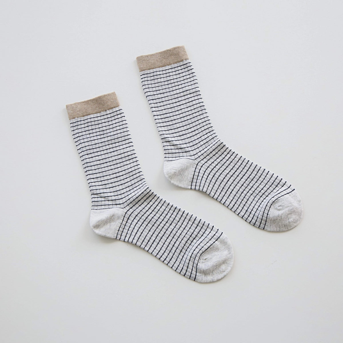 A pair of crew socks with thin black horizontal stripes on a white base, featuring a solid beige ribbed cuff and toe.