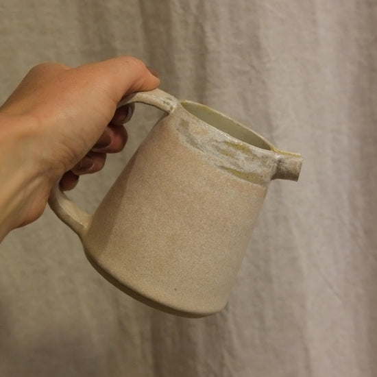 Hand holding a beige ceramic mug against a textured beige background
