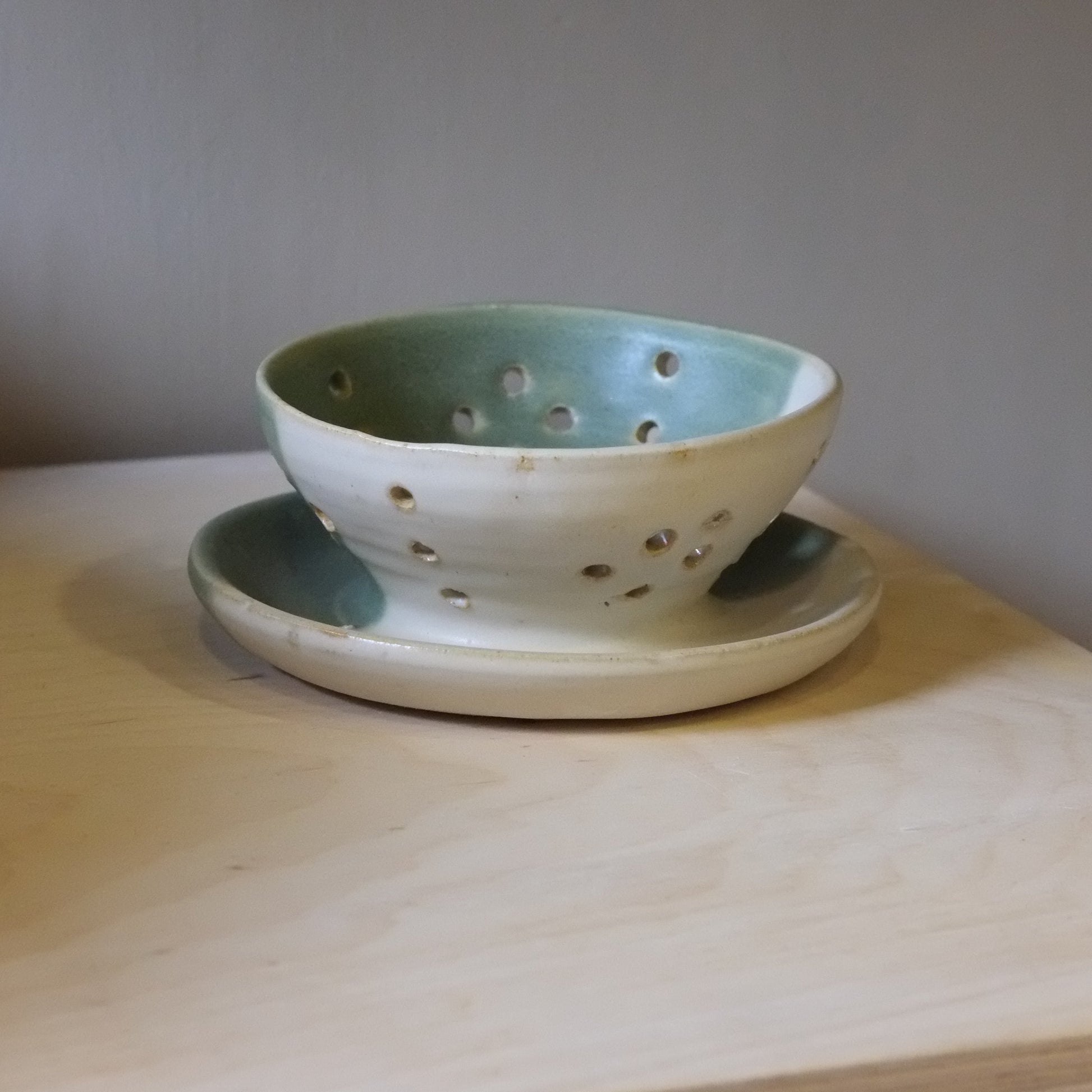Green ceramic colander on a wooden surface with a neutral background