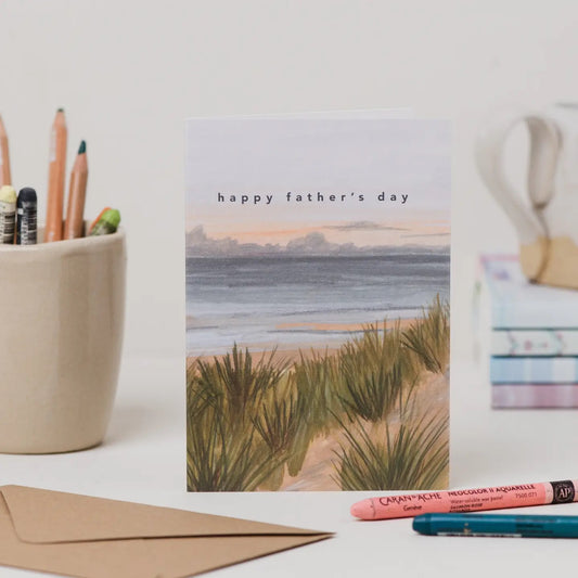 Father's Day card with beach scene, stationery items on a white surface
