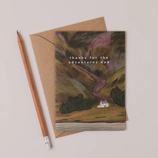 Greeting card with nature-themed illustration and 'thanks for the adventures dad' text, accompanied by a Kraft paper envelope and pencil on a beige background.