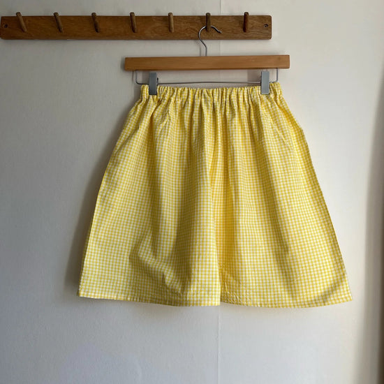 Yellow checkered shorts hanging on a wooden hanger against a white wall.