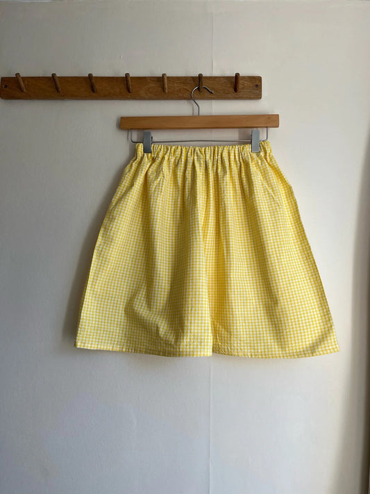 Yellow checkered shorts hanging on a wooden hanger against a white wall.