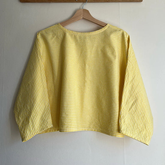 Yellow checkered shirt on a hanger against a white wall with a wooden rack above.