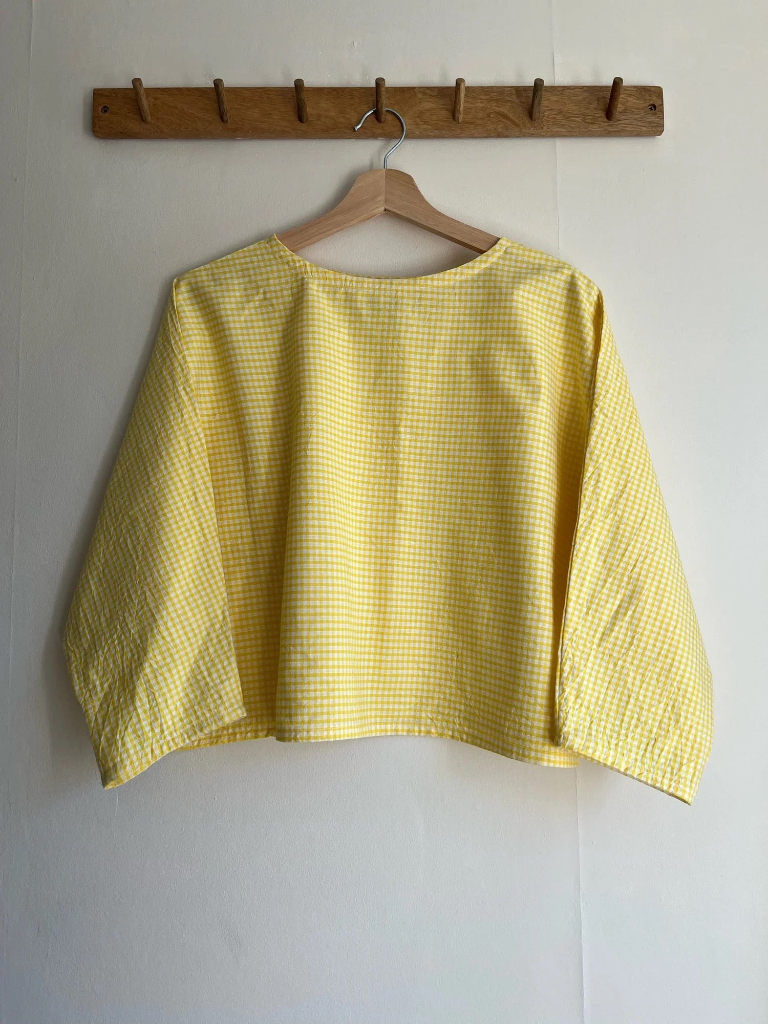Yellow checkered shirt on a hanger against a white wall with a wooden rack above.