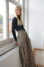 Load image into Gallery viewer, A woman leaning by a window wearing a black top and striped black and white trousers 
