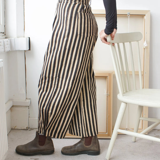 Woman wearing black and white striped trousers leaning on a white chair 
