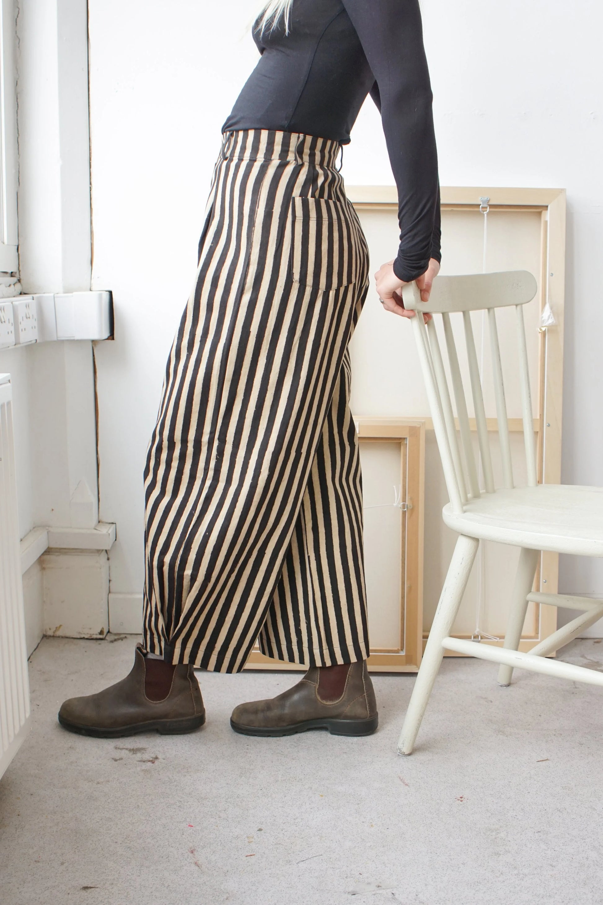Woman wearing black and white striped trousers leaning on a white chair 