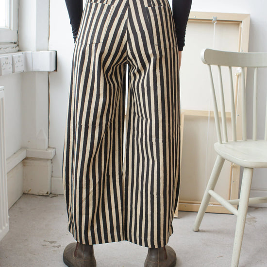 woman wearing long black and white striped trousers facing the wall