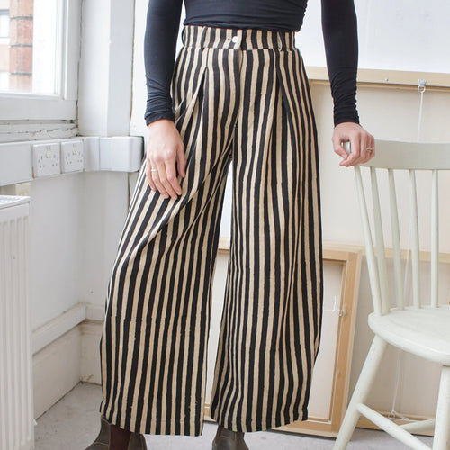 Person wearing black and beige striped pants in a room with a white chair and window.