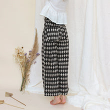 Load image into Gallery viewer, Woman standing by a white wall with heavily patterned trousers on

