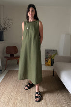 Load image into Gallery viewer, Woman wearing a green linen maxi dress standing in a room with a couch and chair.
