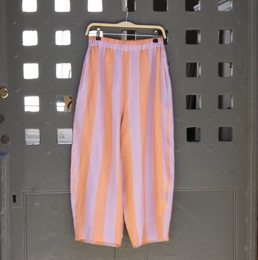 photo of striped balloon style linen trousers in purple and peach hanging on a grey door