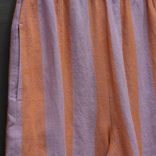 close up photo of detail of some striped linen trousers in lavender and peach showing a side pocket and elasticated waistband 