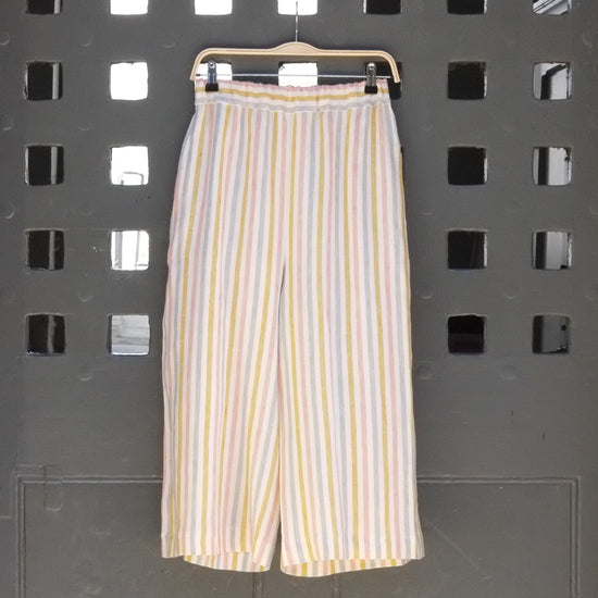 Photo of striped wide leg trousers in pastel colours hanging on a grey door