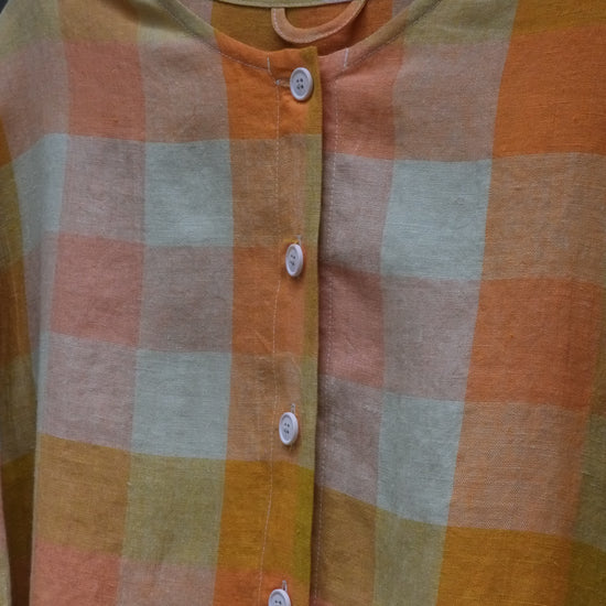 close up photo of a checked collarless shirt with white buttons