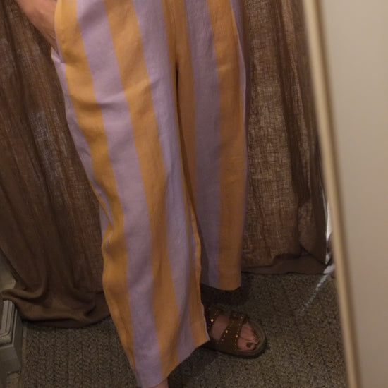 A person wearing wide-leg striped pants with alternating yellow and light lavender-purple stripes, paired with brown studded sandals, shown in a mirror selfie.
